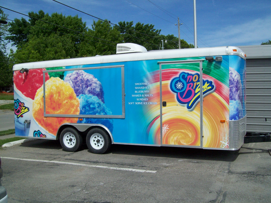 SnoBiz shaved ice trailer parked outside, painted with a rainbow snowball design
