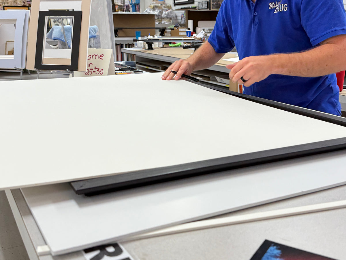 Framer cutting mat board at the custom framing table inside Mahaska Drug