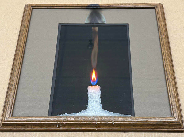 Framed photograph of a lit candle standing on ice, matted in grey